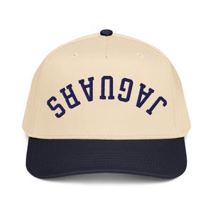 May include: A baseball cap with a cream-colored crown and a navy blue brim. The word "JAGUARS" is embroidered in navy blue across the front. The cap has a curved brim and a button on top.