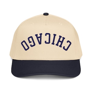 May include: A baseball cap with a cream-colored crown and a navy blue brim. The word "CHICAGO" is arched across the front in navy blue lettering. The cap has a black button on top.
