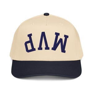 Peut inclure: Casquette de baseball avec une couronne crème et une visière bleu marine. Le mot "MVP" est brodé en bleu marine sur le devant. La casquette a une visière incurvée et un bouton sur le dessus.