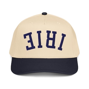 May include: A baseball cap with a cream-colored crown and a navy blue brim. The word "IRIE" is embroidered in navy blue block letters across the front of the cap. The cap has a black button on top.