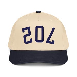 Peut inclure: Casquette de baseball avec une couronne crème et une visière bleu marine. Le numéro "204" est brodé en bleu marine sur le devant. Le chapeau a un bouton noir sur le dessus.