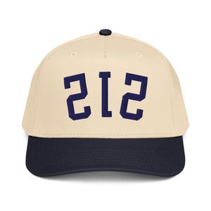 Pode incluir: Um boné de beisebol com uma coroa creme e uma aba azul marinho. O número "212" é exibido em letras de bloco azul marinho na frente do boné. O boné tem uma aba curva e um botão na parte superior.