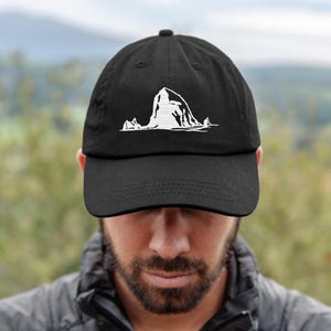 May include: Black baseball cap with a white graphic of a mountain range. The cap has a curved brim and a fabric strap closure. The hat is made of a durable material and is suitable for outdoor activities.