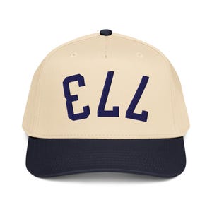 Pode incluir: Boné de beisebol com coroa creme e aba azul marinho. O boné apresenta o número "773" em letras maiúsculas azul marinho na frente. O boné tem uma aba curva e um botão na parte superior.