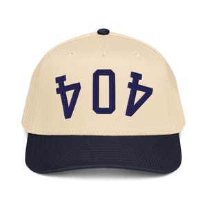 May include: A baseball cap with a cream-coloured crown and a navy blue brim. The cap features the number "404" in navy blue block letters on the front. The cap has a black button on top.