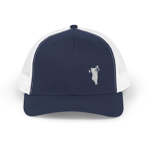 May include: A navy blue trucker hat with a white mesh back and a white embroidered outline of a country's map on the front. The hat has a curved brim and a snapback closure.