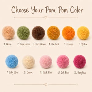May include: A color chart titled Choose Your Pom Pom Color displaying eleven yarn pom poms in various shades: 1. Beige, 2. Sage Green, 3. Dark Brown, 4. Mustard, 5. Orange, 6. Yellow, 7. Baby Blue, 8. Cream, 9. Blush Pink, 10. Soft Pink, 11. Berry Pink.
