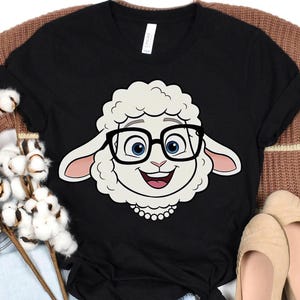 K&ouml;nnte beinhalten: Schwarzes T-Shirt mit einem Cartoon-Schaf mit Brille. Das Schaf hat ein wei&szlig;es Gesicht, blaue Augen und einen l&auml;chelnden Ausdruck. Das T-Shirt besteht aus einem weichen Material und ist f&uuml;r den Freizeitgebrauch geeignet.