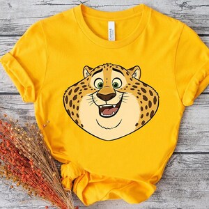K&ouml;nnte beinhalten: Ein gelbes T-Shirt mit einem Cartoon-Leoparden-Gesicht, das l&auml;chelt. Der Leopard hat braune Flecken, gr&uuml;ne Augen und eine hellbraune Nase. Das T-Shirt besteht aus einem weichen Material.