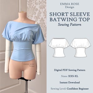 Könnte beinhalten: Hellblaues Kurzarm-Fledermaus-Top auf einer Schneiderpuppe. Das Oberteil hat eine geraffte Taille und einen Off-Shoulder-Ausschnitt. Das Bild enthält eine Schnittmustergrafik mit dem Text "SHORT SLEEVE BATWING TOP Sewing Pattern".