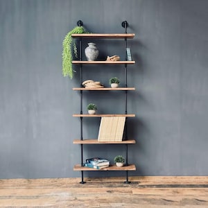 Peut inclure: Une étagère industrielle à cinq niveaux avec des tuyaux en métal noir et des étagères en bois. Les étagères sont décorées de plantes, de livres et de corde.