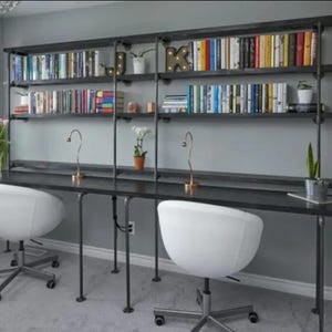 May include: A black metal desk with two white chairs and a black metal shelving unit with books on it. The shelving unit is attached to the wall and has three shelves.