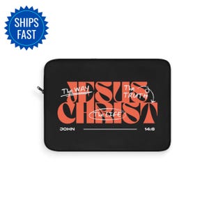 Puede incluir: Funda negra para portátil con las palabras "JESUS CHRIST" en naranja, y las frases "The Way, The Truth, The Life" en blanco. También está presente el texto "JUAN 14:6". La funda tiene un cierre de cremallera.
