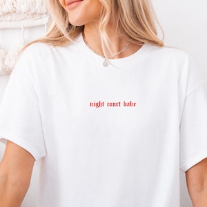 May include: White t-shirt with the text "night court babe" in red.