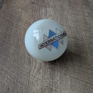 Peut inclure: Un objet sphérique blanc avec le mot "INTERNATIONAL" imprimé en bleu et gris. Il s'agit probablement d'un élément décoratif ou d'une partie d'un produit plus grand.