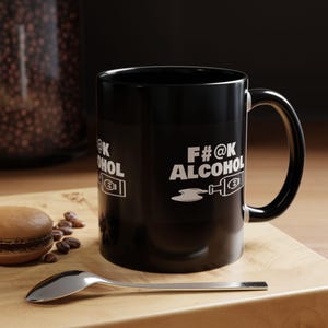 Könnte beinhalten: Schwarze Kaffeetasse mit einer weißen Grafik, auf der "F#@K ALCOHOL" steht, mit einem stilisierten Bild einer Alkoholflasche und einem Tropfen Flüssigkeit.