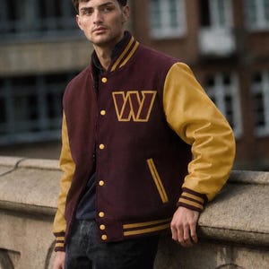 May include: A varsity jacket featuring a deep burgundy wool-blend body and contrasting mustard yellow sleeves. The jacket has a snap-button front closure, ribbed cuffs and hem with yellow stripes, and a large yellow letter W on the left chest.