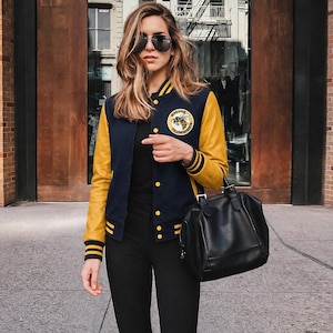 May include: A navy blue and yellow varsity jacket featuring a circular patch on the left chest with a bee illustration and the text Wiskayok Yellowjackets. The jacket has long yellow sleeves, a snap-button front, and striped ribbed cuffs.