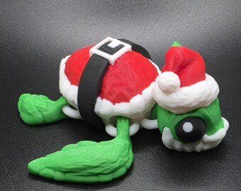 May include: A 3D-printed Christmas turtle figurine. The turtle's shell is red with a white trim and a black belt. The turtle's head is green and wears a Santa hat. The turtle's legs and tail are green.