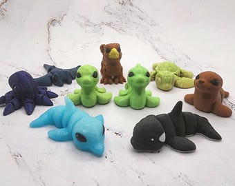 May include: A collection of handmade polymer clay figurines depicting various sea creatures and animals. The assortment includes an octopus, shark, dolphin, orca, turtle, seal, and a bird. The figurines are in various colors, including blue, green, brown, and black.