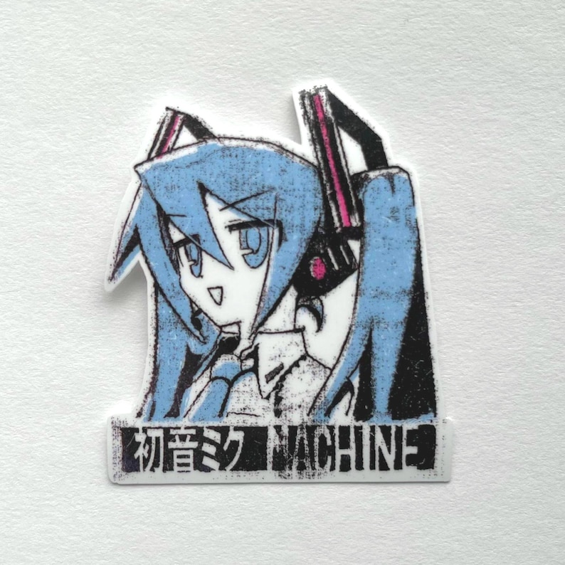 Pu&ograve; includere: Un adesivo in bianco e nero con un personaggio anime dai capelli blu che indossa delle cuffie. Il personaggio ha occhi grandi e un'espressione sorpresa. Il testo "初音ミク MACHINE" &egrave; stampato sotto il personaggio.