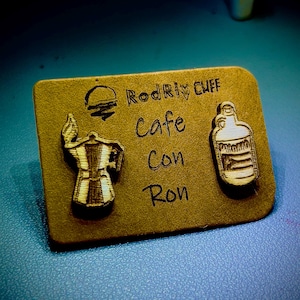 Könnte beinhalten: Ein braunes Holzschild mit dem Text "Rodri Ciff Cafe con Ron" und zwei Holzausschnitten, einer von einer Kaffeekanne und einer von einer Flasche.