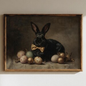 May include: A framed vintage-style painting featuring a black rabbit wearing a gold bow tie, surrounded by decorated Easter eggs. The artwork has a muted color palette with a focus on the rabbit and eggs.