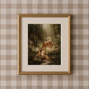 May include: Framed art print featuring a serene forest scene with a deer drinking from a stream. The artwork is set in a gold frame and has a cream-colored mat. The background is a beige and white checkered pattern.