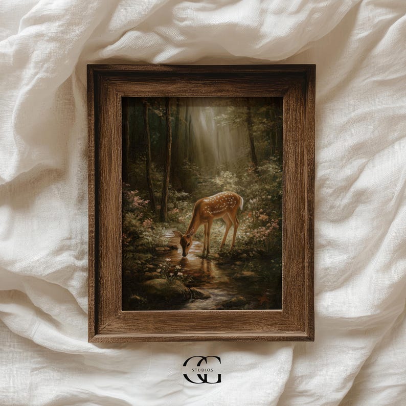 May include: A framed print featuring a serene forest scene with a deer drinking from a stream. The artwork is set in a dark brown wooden frame. The deer has brown fur with white spots. The forest is lush with green foliage and sunlight.