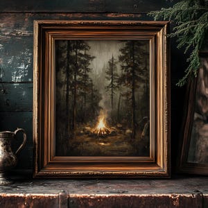 Könnte beinhalten: Gerahmtes Landschaftsgemälde, das ein Lagerfeuer in einem dunklen Wald zeigt. Das Kunstwerk ist in einem Holzrahmen mit warmem, braunem Finish gefasst. Die Szene ist in gedämpften Tönen gehalten, wobei das Feuer die Hauptlichtquelle darstellt.
