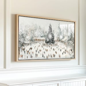 May include: A framed winter scene print depicting a snowy outdoor gathering. The artwork features a large Christmas tree, people, and buildings, all set against a backdrop of falling snow and snowflakes. The frame is a light wood color.