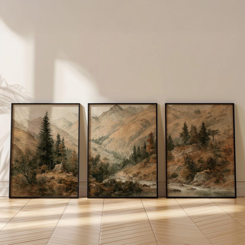 Op de afbeelding: Set van drie ingelijste landschapskunstprints. Elke print toont een aquarel schilderij van een berglandschap met bomen en een rivier. Het kleurenpalet omvat tinten bruin, groen en beige.