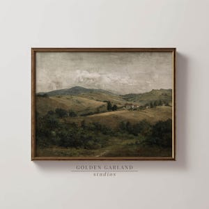May include: A framed landscape painting showing rolling hills and a distant mountain range under a cloudy sky. The artwork uses a muted palette of greens, browns, and greys, with a wooden frame. The text "GOLDEN GARLAND studios" is at the bottom.