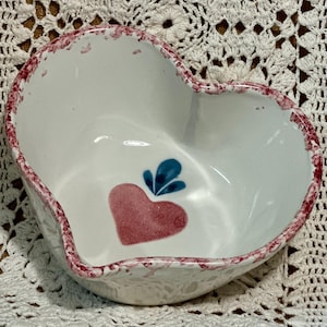 Może przedstawiać: Ceramiczna miska w kształcie serca z białym wnętrzem i czerwonym, nakrapianym brzegiem. Miska ma czerwony wzór serca z niebieskimi liśćmi. Ta dekoracyjna miska jest idealna do serwowania przekąsek lub jako uroczy element akcentujący.