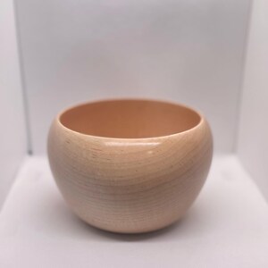 May include: A light brown wooden bowl with a rounded shape. The bowl is empty and appears to be made of a smooth wood.