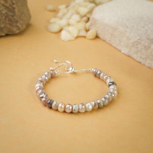 May include: A silver adjustable bracelet with a string of faceted, light brown, gray, and white beads.