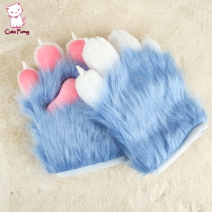 以下が含まれることがあります： ピンクと白の肉球が付いた青い毛皮の手袋人形のペア。人形は手首の開口部に白いフェルトの裏地が付いています。