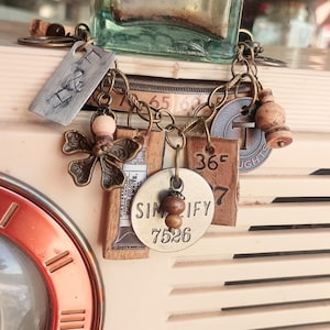 Puede incluir: Un brazalete con charms con una variedad de charms, incluyendo una mariposa, un tapón de botella, una etiqueta que dice "Simplify 7526" y una etiqueta que dice "36°F".