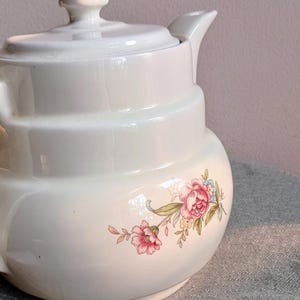 Puede incluir: Tetera de cerámica color crema con tapa y boquilla. La tetera presenta un diseño floral con flores rosas y verdes. Un diseño clásico, adecuado para servir té.