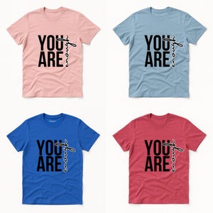 May include: Four t-shirts in pink, blue, light blue, and red. Each shirt has the words "YOU ARE" in bold black font, with "enough" written in a cursive font.