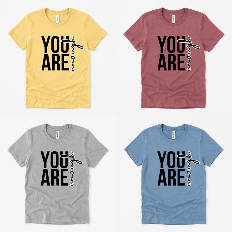 May include: Four short-sleeved t-shirts in yellow, burgundy, gray, and blue. Each shirt features the text "YOU ARE" in a bold, black font, with "enough" written in a script font. The shirts are displayed on a white background.