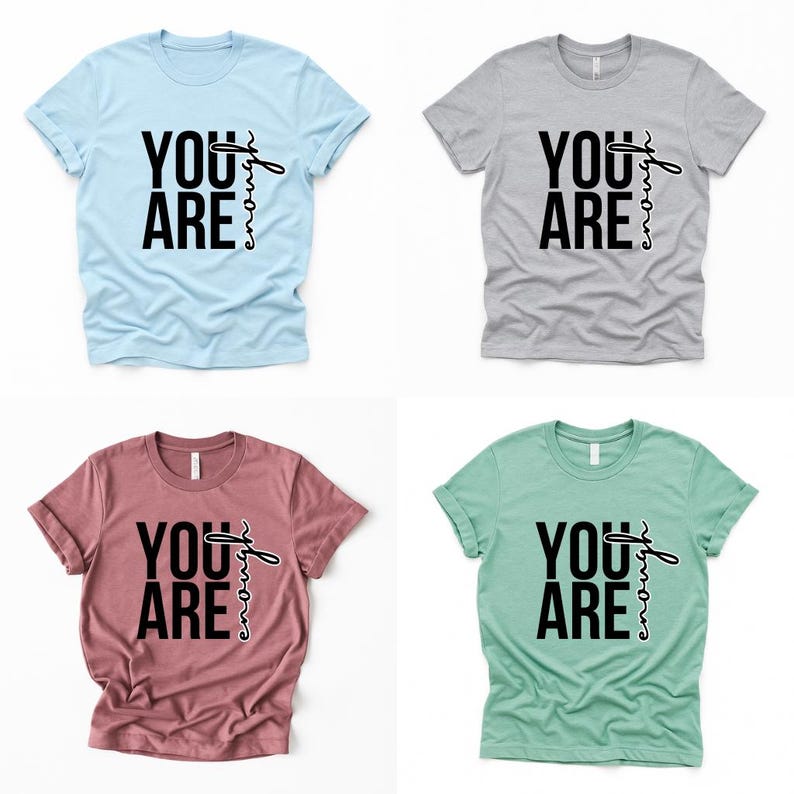 May include: Four short-sleeved t-shirts in light blue, gray, mauve, and mint green. Each shirt features the words "YOU ARE" in bold black letters, with "enough" written in a cursive font.
