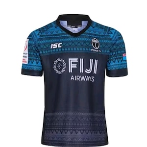 May include: A blue and black Fiji Airways rugby shirt. The shirt has a patterned design on the shoulders and sleeves, with the text "FIJI AIRWAYS" across the chest. The shirt also features the text "FIJIAN 7s" and the Fiji flag.