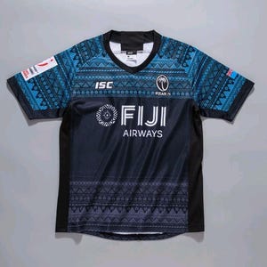 Puede incluir: Una camiseta de rugby Fiji Airways azul marino y turquesa. La camiseta presenta un cuello en V, mangas cortas y un patrón geométrico en los hombros y las mangas. Las palabras "FIJI AIRWAYS" están impresas en blanco en la parte delantera.