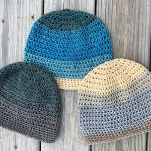 May include: Three crocheted hats in different color combinations. The hats are made with a variety of shades of blue, green, gray, and brown yarn.