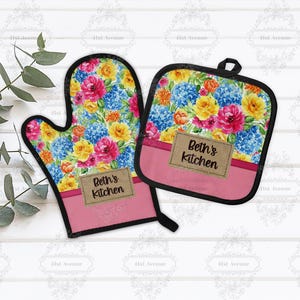 May include: A floral oven mitt and pot holder set. The mitt and pot holder feature a colorful floral pattern with pink, blue, and yellow flowers. The set includes the text "Beth's Kitchen" on a brown label.
