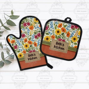 Peut inclure: Un ensemble de manique et de gant de cuisine à motifs floraux. Le gant et le dessous de plat présentent un motif coloré de tournesols, de coquelicots et d'autres fleurs. Le texte "Beth's Kitchen" est affiché sur une étiquette marron sur les deux articles.