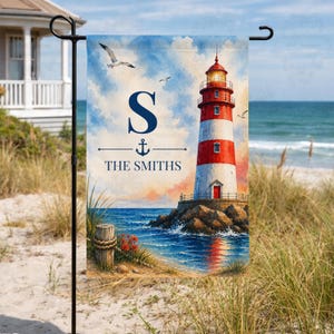May include: A rectangular garden flag featuring a watercolor illustration of a red and white lighthouse on a rocky shore. The design includes a large navy blue letter S, a small anchor icon, and the text THE SMITHS, with seagulls in the sky.