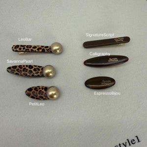 Peut inclure: Plusieurs barrettes à cheveux de différents modèles. Certaines présentent un motif léopard avec un accent perlé doré. D'autres sont marron uni avec les inscriptions "SignatureScript", "Calligraphy" et "EspressoBijou".
