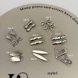 May include: A selection of silver hair accessories, including barrettes, bow-shaped clips, and heart-shaped pins. Some pieces feature rhinestones or colourful polka dots. The text "Many poets and artists have draw" and "style1" are visible.
